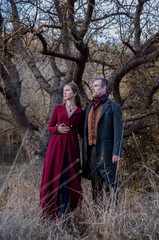 Vampire woman wearing in a burgundy coat holding lantern in autumn forest. Victorian style vintage