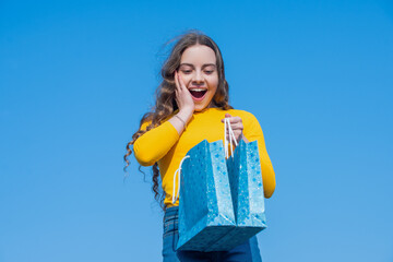 surprised teen girl opening shopping bag, blue yellow