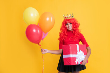 smiling teen child in crown with present box and party balloon on yellow background