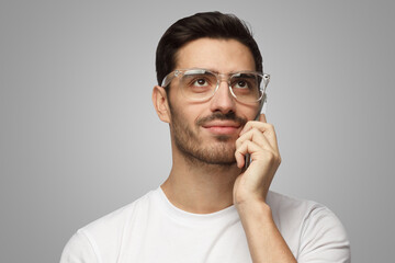Closeup headshot of man on gray background in glasses looking up while talking on phone thinking