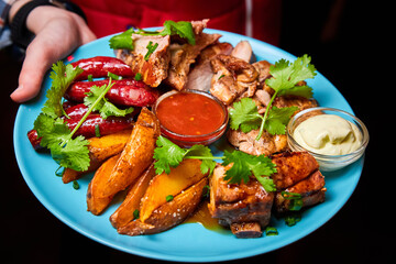 Waiter holding a large platter with Shish kebab, grilled potato and sauces. Close-up, selective focus