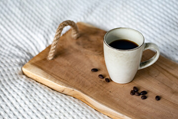 Cup of dark strong coffee and roasted coffee beans on wooden tray in bed in the morning