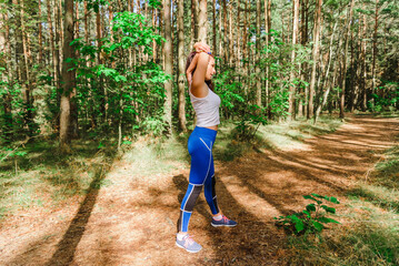 Young pretty Woman stretching arms and breathing fresh air in a summer forest while exercising. Workouts and Lifestyles concept. Healthy life and Healthcare theme.Nature and Outdoors concept.