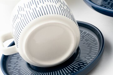 Closeup shot of a blue and white mug on a saucer with a white background.