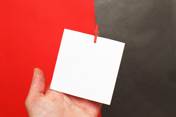 human hand holding sticker with empty mockup for text hanging on pin on red and black background.