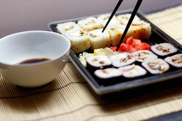 Foto op Plexiglas Set of red ginger rolls with a soy sauce bowl on a bamboo mat © Ruslan Kolodenskiy/Wirestock Creators