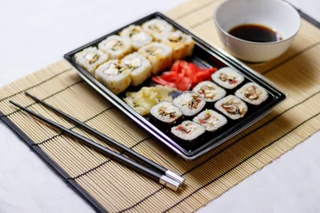 Fotobehang Set of red ginger rolls with a soy sauce bowl and black chopsticks on a bamboo mat © Ruslan Kolodenskiy/Wirestock Creators