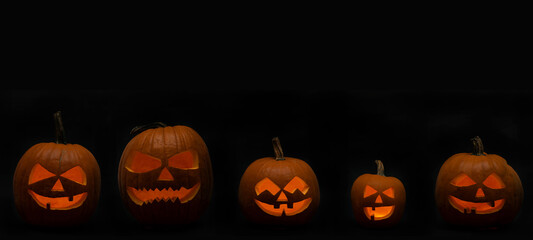 Scary Halloween celebration holiday card banner panorama  - Many spooky carved glowing pumpkins in the dark night, isolated on black background