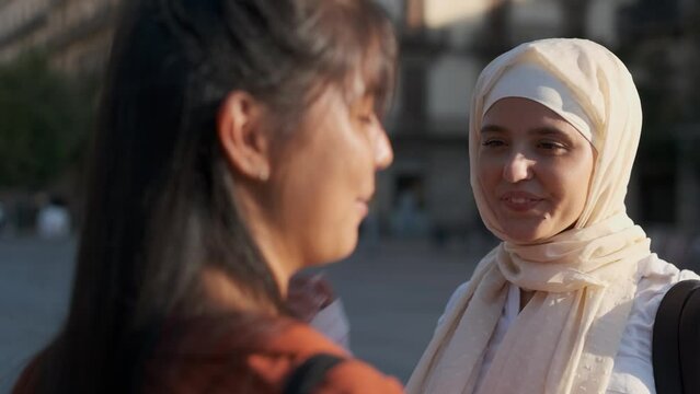 Young arab woman in hijab smiling while talking with a friend outdoors on the street.