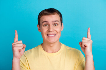 Portrait of a young man wear t-shirt pointing fingers away copy space isolated over blue background