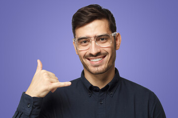 Guy isolated on purple background, showing gesture as if asking to dial him, looking confident