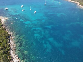 Aerial view of Cala Moresca and Figarolo Island in Golfo Aranci, north Sardinia. Birds eye from above of yacht, boats, crystalline and turquoise water. Tavolara Island in the background, Sardegna.