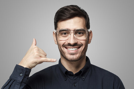 Young man showing gesture as if asking to calll him, looking confident, isolated on gray