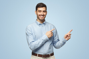Smiling young business man pointing away, isolated on blue background