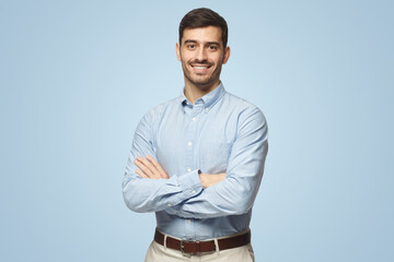 Handsome smiling business man in blue shirt standing with crossed arms on blue background