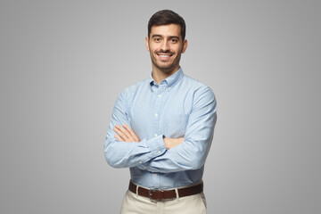 Handsome business man in blue shirt standing with crossed arms on gray background - 535762779