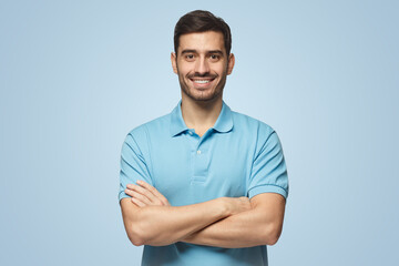 Smiling handsome man in blue polo shirt standing with crossed arms on blue background