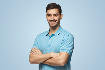 Portrait of young sporty man in blue polo shirt standing with crossed arms, isolated on blue
