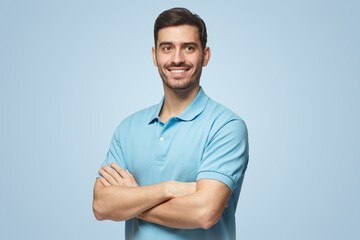 Smiling handsome young man in polo shirt standing with crossed arms, isolated on blue background