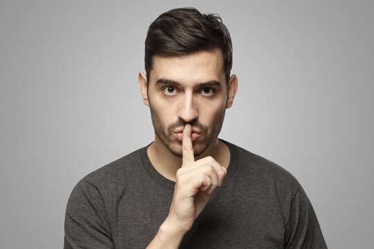 Man dressed in casual t-shirt, pressing finger to lips as if asking to keep silence