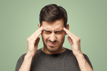 Man suffering from headache, pressing fingers to temples with closed eyes on green background - obrazy, fototapety, plakaty