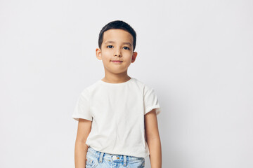a little boy of preschool age stands on a white background in a white T-shirt and blue jeans, smiling a little and putting his hands down