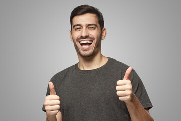 Young man showing thumbs up with positive emotions and happiness, isolated on gray background