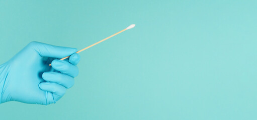 Cotton stick for swab test in hand with blue latex glove on mint green or Tiffany Blue background.