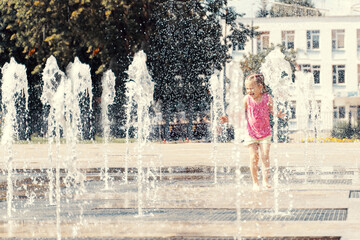 happy child playing with water splashes in city fountain