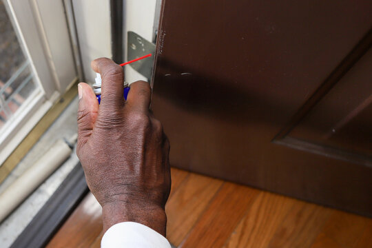 A Black African-American Man Spraying Lubricant In A Door Hinge