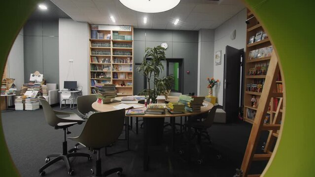 Bookcase with round hole and table with different literature in stylish children library. Elegant books storage in school