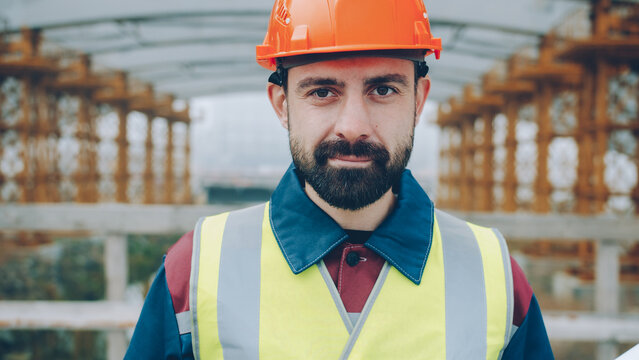 Portrait of confident construction workman wearing safety uniform standing in building area and looking at camera. People and occupation concept.