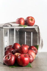 Ripe red apples in a wooden box on a stone table, front view, white background with copy space. Selective focus on the front