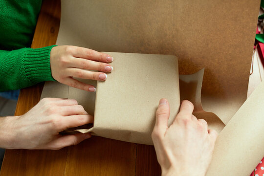 Close-up image of man's and woman's hands wrapping christmas presents at home. Holiday preparation. Self made decorations