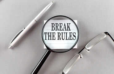 Word BREAK THE RULES on sticky through magnifier on grey background