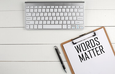 Home office workspace with keyboard, clipboard and pen with text WORDS MATTER on white wooden...