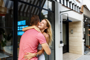 Farewell concept. Delighted happy smiling blonde woman says goodbye or hi to boyfriend, gives warm hug, pose together against cafe place. Truthful feelings