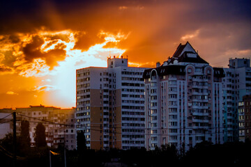 Fototapeta na wymiar A burning multi-colored sunset among the clouds sits behind the houses of the city 