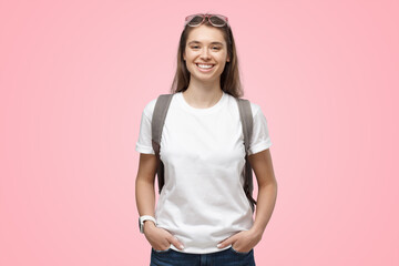 Smiling girl wearing white t-shirt and backpack, isolated on pink