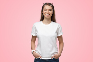Young woman with hands in pockets, wearing blank white t-shirt with copy space on pink background