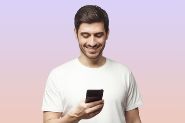 Closeup of man holding phone in hand smiling happily looking at screen on pink background