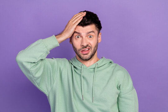 Photo of young funny excited nervous unhappy man wear khaki hoodie touch his head forget oops house keys grimace isolated on violet color background