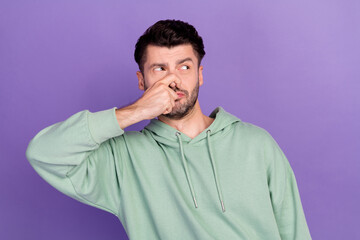 Portrait photo of young funny unhappy student man wear khaki sweater close his nose smell stink look empty space object isolated on violet color background