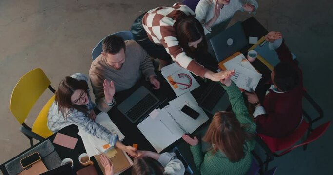 Top view group of happy business partners high five each other celebrating team success at office table slow motion.