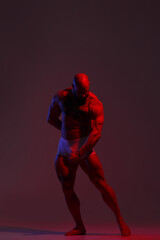 Athletic man demonstrates muscles in the light of a red light filter on a dark background.