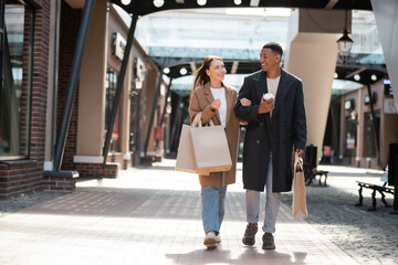 smiling woman with shopping bags talking to african american boyfriend while walking on city street. - Powered by Adobe