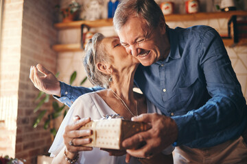 Elderly, couple and happy with gift, surprise and kiss on face together in home. Man, woman and...