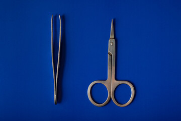 Scissors and tweezers isolated on a blue background.