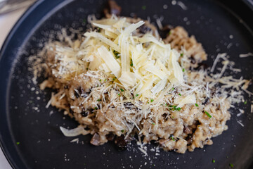 Grated parmesan cheese on top of mushroom risotto on black plate. Healthy vegetarian menu, fancy restaurant concepts