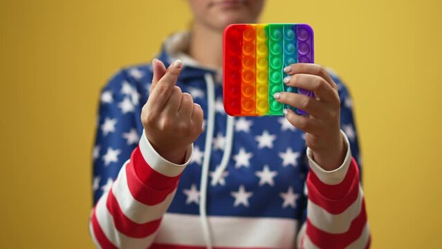 Unrecognizable Caucasian woman with multicolored fidget toy showing cash gesture. Young lady posing at yellow background with trendy sensory toy. Slow motion